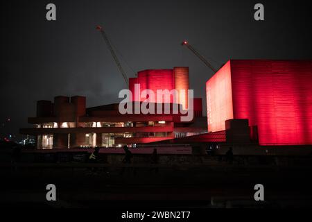 Les navetteurs rentrent chez eux une nuit d'hiver à travers Waterloo Bridge à côté d'un théâtre national rouge illuminé bankside, Southbank, centre de Londres, Angleterre. Banque D'Images