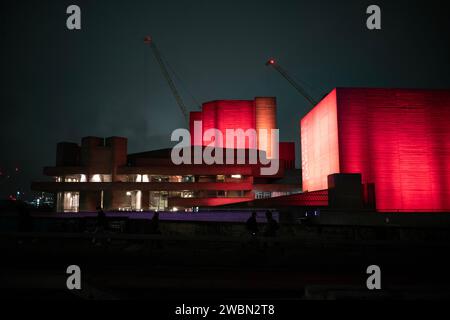 Les navetteurs rentrent chez eux une nuit d'hiver à travers Waterloo Bridge à côté d'un théâtre national rouge illuminé bankside, Southbank, centre de Londres, Angleterre. Banque D'Images