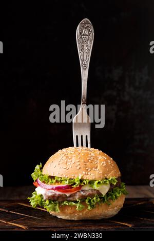 Hamburger appétissant frais avec du bœuf sur un fond sombre, fourchette vintage dans un hamburger. Banque D'Images