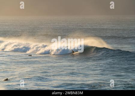 Un surfeur émerge avec le soleil à Ho'okipa, creusant un chemin à travers les vagues immaculées du matin de Maui. Banque D'Images