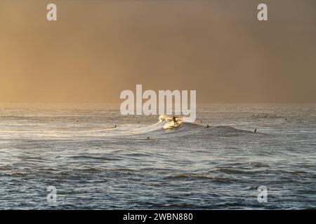 Les surfeurs glissent sur les vagues scintillantes tandis que les rayons dorés du soleil couvrent Ho'okipa, un sanctuaire pour surfeurs. Banque D'Images