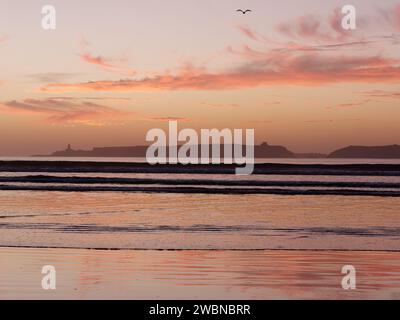 Nuages rouges au coucher du soleil au-dessus d'une île alors qu'un oiseau vole au-dessus d'Essaouira, Maroc, 11 janvier 24 Banque D'Images