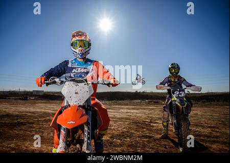 Rétro-éclairage de deux coureurs de motocross face à l'avant posant avec un autre cavalier sautant en arrière-plan. Banque D'Images