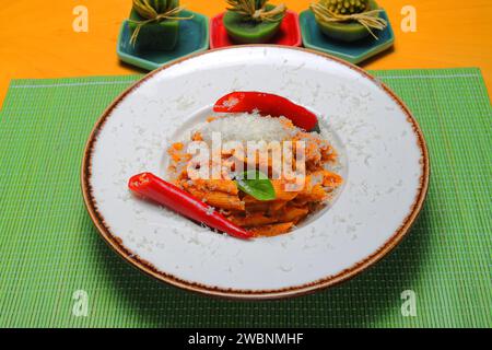 Pène alla arrabiata, pâtes à la sauce rouge italienne servies sur une table dans une assiette avec une râpe fraîche de parmesan. Banque D'Images