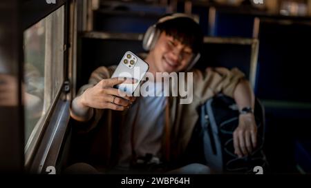 Un jeune asiatique heureux prend des selfies avec son smartphone alors qu'il est dans un train quelque part en Asie. voyageur solo, vacances, backpacker Banque D'Images