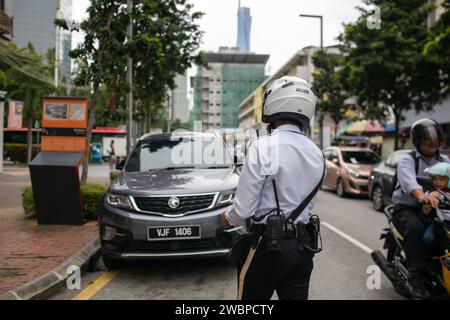 Kuala Lumpur, Malaisie - 8 janvier 2024 : un agent de la police de la circulation photographie et délivre des billets aux propriétaires de véhicules stationnés illégalement. Banque D'Images