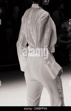 Mannequin portant un chemisier à manches longues blanc transparent avec des rayures blanches et un pantalon blanc vu de derrière au Raffles Graduate Runway Fashion Show Banque D'Images