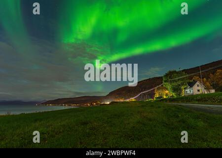Belles aurores boréales vertes sur un fjord et une maison sur l'île de Kvaloya près de Tromsø. danser des lumières polaires au-dessus d'une montagne, aurora borealis Banque D'Images