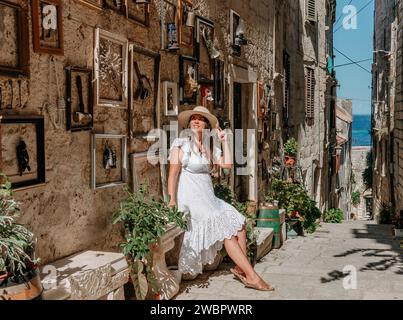 Une femme élégante enfilant une robe blanche immaculée et un chapeau se relaxant dans une ruelle pittoresque Banque D'Images