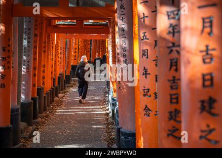 Voyageur marchant à travers les portes torii au sanctuaire Fushimi Inari à Kyoto, Japon. Banque D'Images