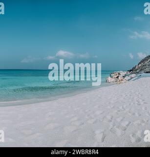 Sable blanc immaculé et eaux turquoise limpides à Shoab Beach, Socotra, Yémen, sous un ciel bleu vif. Banque D'Images