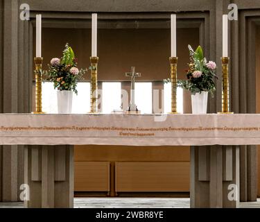 Croix placée sur une surface de pierre avec inscription près des fleurs et des bougies dans des vases à l'intérieur de l'église Hallgrimskirkja située à Reykjavik Banque D'Images