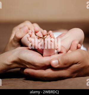 Maman et papa tiennent les jambes de leur enfant, des anneaux de mariage en or sur les orteils. Banque D'Images