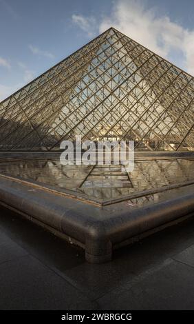 France, Paris - Jan 03, 2024 - devant le célèbre musée du Louvre et sa grande pyramide de verre pendant la journée avec effet de réflexion de l'eau par After Banque D'Images