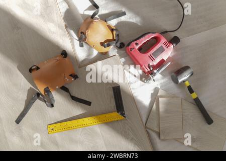 Marteau en caoutchouc, règle avec barre d'angle, mètre à ruban, scie sauteuse et autres outils pour l'installation du sol en vinyle stratifié. Amélioration de la maison, nouvelle installation de plancher Banque D'Images