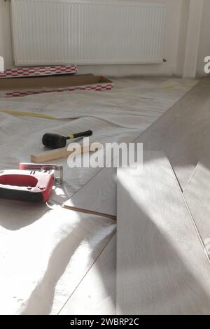 Marteau en caoutchouc, règle avec barre d'angle, mètre à ruban, scie sauteuse et autres outils pour l'installation du sol en vinyle stratifié. Amélioration de la maison, nouvelle installation de plancher Banque D'Images