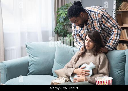 Couple de race mixte homme afro-américain et femme blanche, homme masser sa petite amie ou sa femme dans sa période menstruelle tout en étant assis à la maison. Amour, suppo Banque D'Images