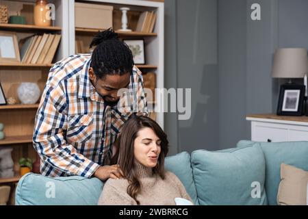 Couple de race mixte homme afro-américain et femme blanche, homme masser sa petite amie ou sa femme dans sa période menstruelle tout en étant assis à la maison. Amour, suppo Banque D'Images