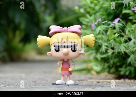 Funko Pop figurine d'action de Helga Pataki de la série télévisée d'animation Nickelodeon Hey Arnold. Jouet debout sur la route asphaltée dans le parc de printemps, fleurs roses. Banque D'Images