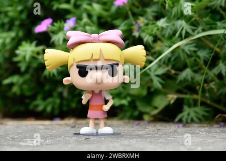 Funko Pop figurine d'action de Helga Pataki de la série télévisée d'animation Nickelodeon Hey Arnold. Jouet debout sur la route asphaltée dans le parc de printemps, fleurs roses. Banque D'Images