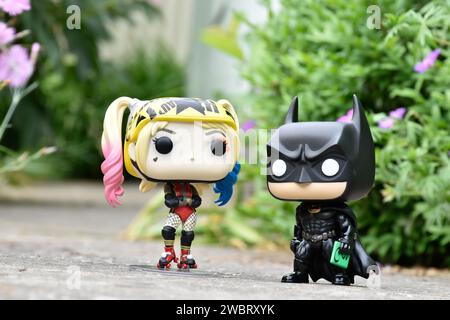 Funko Pop figurines d'action de DC comics super-héros Harley Quinn et Batman debout sur la route asphaltée dans le parc de printemps, herbe verte, fleurs roses. Banque D'Images