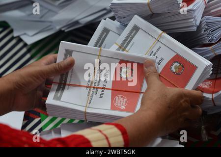 Magelang, Java central, Indonésie. 11 janvier 2024. Un travailleur plie des bulletins de vote et montre des photos de candidats à la présidence sur des bulletins de vote pour l'élection présidentielle du 14 février montrant les candidats, de gauche à droite, Anies Baswedan et son coéquipier Muhaimin Iskandar, Prabowo Subianto et son coéquipier Gibran Rakabuming Raka, et Ganjar Pranowo et son coéquipier Mahfud MD, lors des préparatifs pour la distribution de la logistique électorale à Magelang, Java central, le 11 janvier 2024. La troisième plus grande démocratie du monde a établi la liste électorale permanente (DPT) pour l'élection générale de 2024 à 20 Banque D'Images