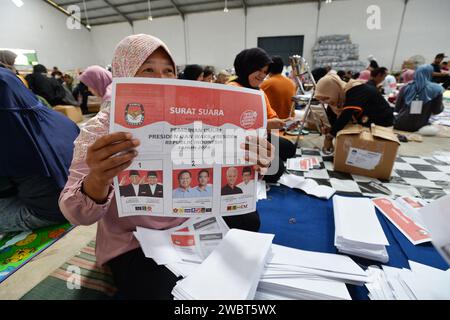 Magelang, Java central, Indonésie. 11 janvier 2024. Un travailleur plie des bulletins de vote et montre des photos de candidats à la présidence sur des bulletins de vote pour l'élection présidentielle du 14 février montrant les candidats, de gauche à droite, Anies Baswedan et son coéquipier Muhaimin Iskandar, Prabowo Subianto et son coéquipier Gibran Rakabuming Raka, et Ganjar Pranowo et son coéquipier Mahfud MD, lors des préparatifs pour la distribution de la logistique électorale à Magelang, Java central, le 11 janvier 2024. La troisième plus grande démocratie du monde a établi la liste électorale permanente (DPT) pour l'élection générale de 2024 à 20 Banque D'Images