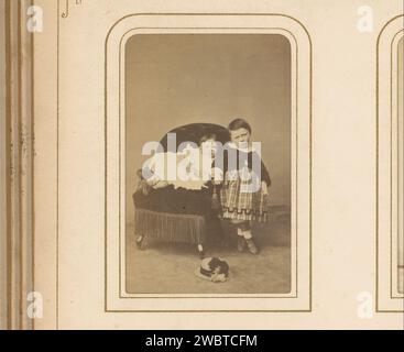 Portrait d'un bébé sur une chaise et d'une fille debout, avec un chapeau au premier plan, Adrien Barboni, 1859 - 1866 Photographie. Carte de visite cette photo fait partie d'un album. Brussels Cardboard. Support photographique albumen print personnes historiques - BB - femme. bébé, bébé  les âges de l'homme. chaise. tout-petits (femmes) Banque D'Images