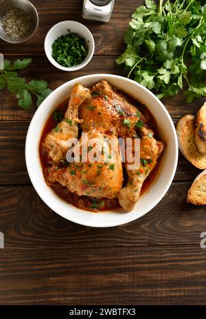 Ragoût de poulet géorgien avec tomates et herbes (chakhokhbili) dans un bol sur fond en bois avec espace libre pour le texte. Viande de poulet cuite au four avec tomate v Banque D'Images