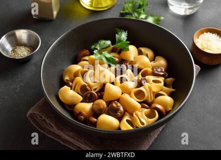 Pâtes Pipe rigate aux champignons rôtis servies dans un bol noir sur fond de pierre sombre. Gros plan Banque D'Images