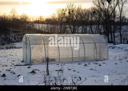 Une serre en hiver dans le village. Soirée et lever du soleil sur des arbres sans feuilles Banque D'Images