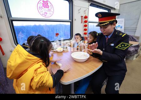 (240112) -- HARBIN, 12 janv. 2024 (Xinhua) -- le chef d'orchestre Zhao Zihe fabrique des boulettes avec des enfants de la région autonome de Guangxi Zhuang dans le sud de la Chine sur le train K7042, un train qui part de Mohe en direction de Harbin dans la province de Heilongjiang, dans le nord-est de la Chine, le 5 janvier 2024. Ces enfants mignons sont surnommés « petites mandarines à sucre » (une spécialité du Guangxi) par les internautes chinois. Onze enfants d'âge préscolaire de Nanning, la capitale de la région autonome de Guangxi Zhuang, dans le sud de la Chine, ont capturé le cœur des internautes chinois alors qu'ils embarquent dans un camp « courageux » dans le nord-est de la Chine, Banque D'Images