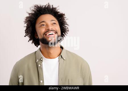 Photo de studio d'heureux jeune homme afro-américain portant un t-shirt décontracté blanc posant isolé sur fond blanc. Homme millénaire souriant levant les yeux Banque D'Images