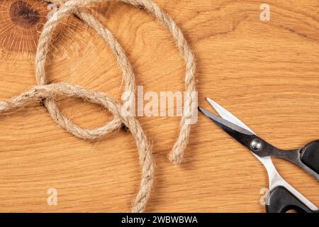 Vue de dessus d'une corde rugueuse soigneusement enroulée avec une paire de ciseaux sur un fond en bois. La corde est épaisse et altérée, créant un f rustique et robuste Banque D'Images