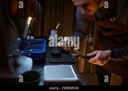 Barista tenant le porte-filtre avec du café moulu et falsifiant dans le café Banque D'Images