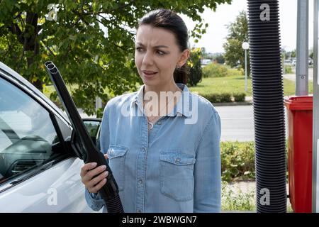 Femme semble surprise à l'extrémité du tuyau d'un aspirateur industriel à une station de lavage de voiture. Concept d'émotion d'étonnement. Banque D'Images