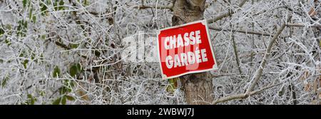 Panneau de chasse rouge dans une forêt couverte de gel, suspendu à un tronc d'arbre Banque D'Images