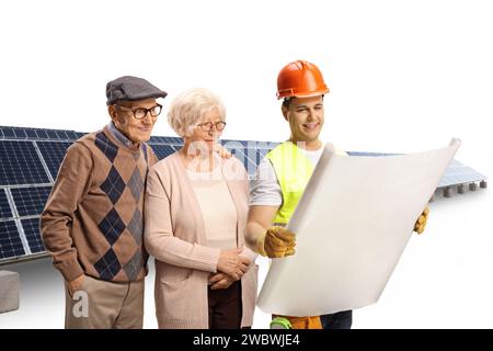 Travailleur de la construction montrant un plan à un couple âgé devant des panneaux solaires isolés sur fond blanc Banque D'Images