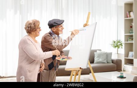 Homme et femme senior peignant avec des pinceaux sur une toile à la maison Banque D'Images