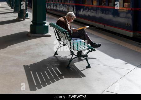 Porto, Portugal-3 octobre 2022 ; homme âgé lisant le journal sur un banc sur la plate-forme ensoleillée de la gare de São Bento Banque D'Images