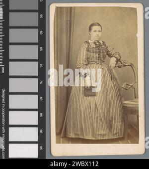 Portrait d'une jeune femme inconnue avec un livre près d'une chaise, Bernardus Petrus Rabels, 1870 - 1893 Photographie. Carte visite Amsterdam Cardboard. papier albumen print adolescent, jeune femme, jeune fille. Une personne historique anonyme a représenté Amsterdam Banque D'Images