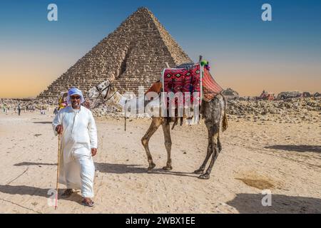 Nécropole de Gizeh, Égypte - 26 avril 2022 : Bédouin vêtu de vêtements traditionnels, tenant un chameau décoré de broderies spécifiques. Banque D'Images