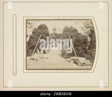 Pont dans le Stadspark les Buttes de Chaumont avec à la fin le temple de la Sibylle à Paris, Anonyme, en ou après 1869 - v. 1900 photographie. Photographie de cabinet partie de l'album photo avec des photos de cabinet de sites à Paris et Versailles. Paris carton. papier. support photographique albumen print jardins publics, parc (+ ville(-paysage) avec figures, personnel). temple, sanctuaire  religion romaine. temple, sanctuaire  religion grecque. Paysage avec pont, viaduc ou aqueduc Paris Banque D'Images