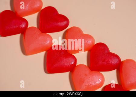 Tableau de deux lignes de bonbons en forme de cœur de pêche et de bonbons gommeux rouges sur un fond orange pastel, se posant en diagonale dans une image horizontale avec du li dur Banque D'Images