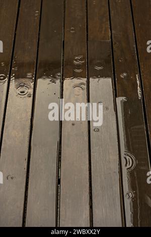 des vagues produites par les gouttes d'eau sur le plancher de planche de bois d'une terrasse remplie d'eau de pluie un jour d'hiver Banque D'Images