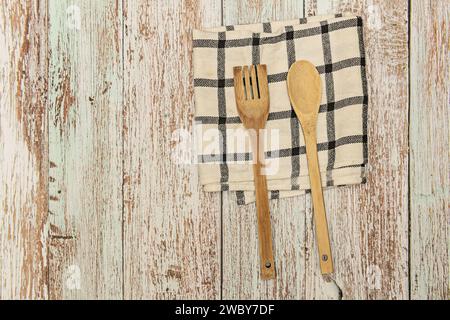 Une cuillère en bois et une fourchette sur un tissu blanc avec des lignes grises sur une surface de planche de bois pelée Banque D'Images