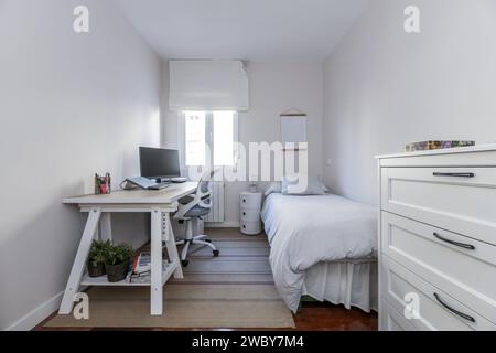 Une chambre de jeunesse avec un lit simple et un bureau madra blanc à côté de la fenêtre Banque D'Images