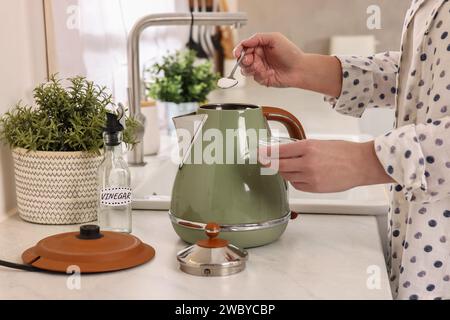 Femme ajoutant du bicarbonate de soude dans une bouilloire électrique dans la cuisine, closeup Banque D'Images