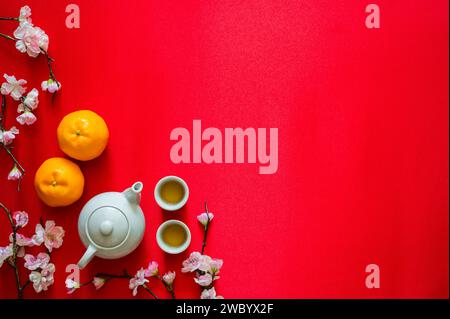 Service à thé avec oranges et fleur de pêche sur fond de tissu rouge pour le concept du nouvel an chinois. Banque D'Images