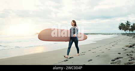 Femme, planche de surf et marche sur le sable à la plage, la mer et l'océan pour les vacances d'été, voyage d'aventure et de bonheur. Surfeur japonais sur le rivage pour Banque D'Images